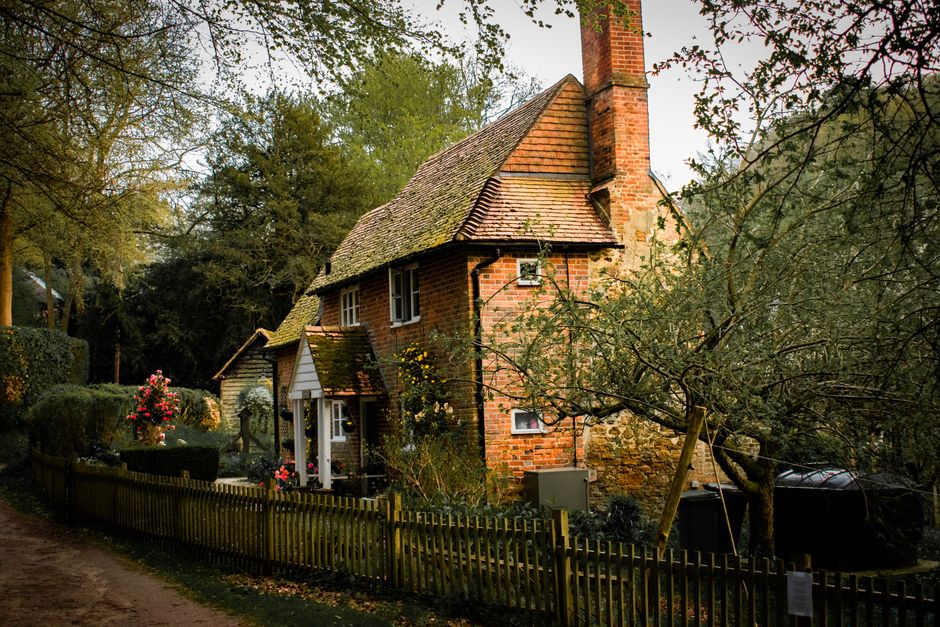 Front view of a traditional English cottage with a distinctive black and white timber-framed facade and white plaster infill. The house features a pitched roof with dark tiles, a white front door flan